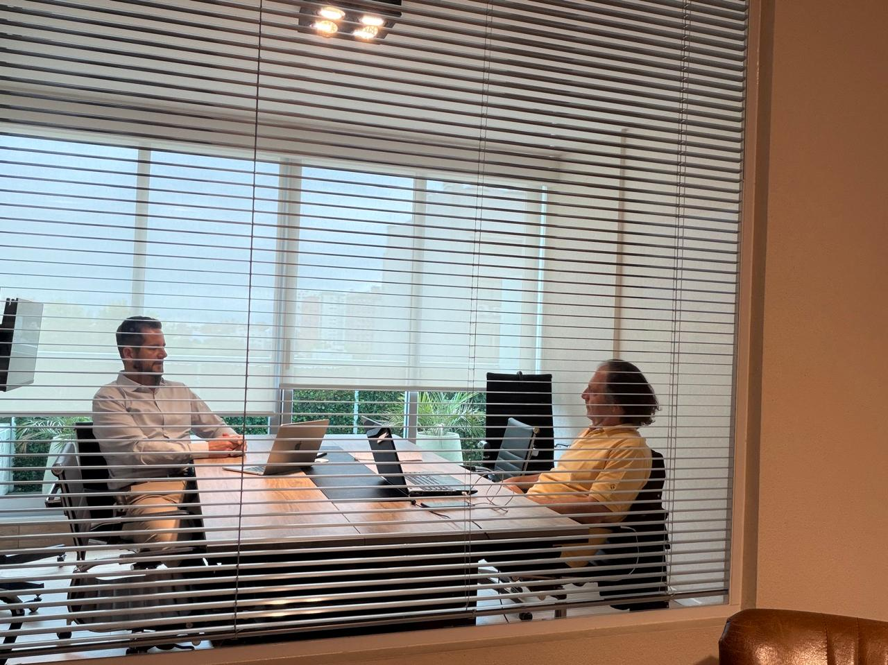 Two people talking across their laptops in a meeting room.